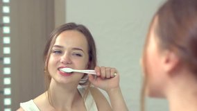 Young attractive woman brushing her teeth with a toothbrush, looking at her white teeth at the mirror and enjoying of her beautiful smile. Slow motion video footage high speed camera 240 fps. 1080p 