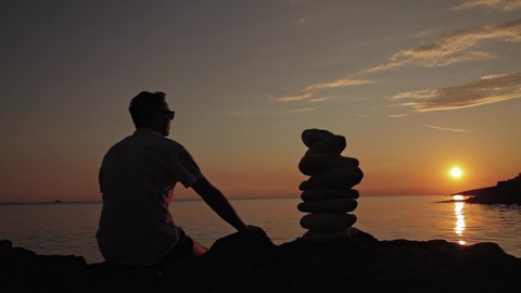 Silhouette of a man and zen stones on a ocean sea cliff in sunset sunrise time.	