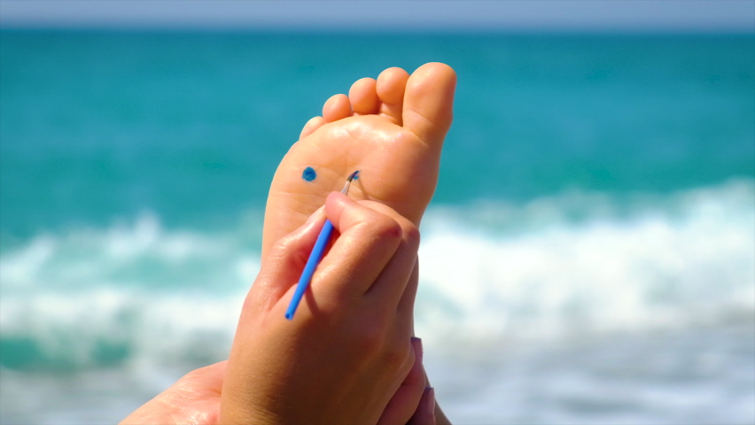 Child feet paint a smile on the beach. Selective focus.