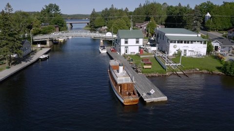 Drone shot of small town of Dorset Ontario with bridges over the river, boats docked and an old wooden ship