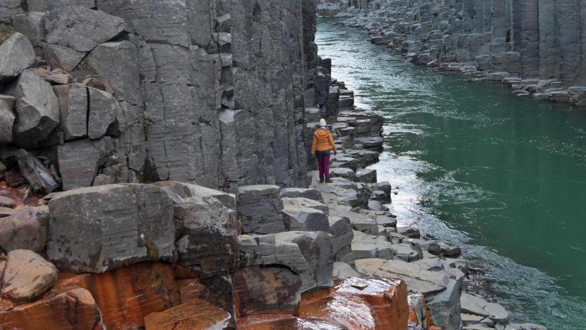 A person walking and looking around on basalt rocks in a canyon with green river and basalt columns