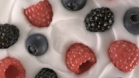 Delicious looking, well crafted fresh yogurt that decorated with fresh black-red raspberries and blueberries rotates in reverse clockwise.