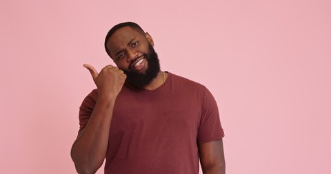 Young African american cheerful man point out with thumb isolated on pink background