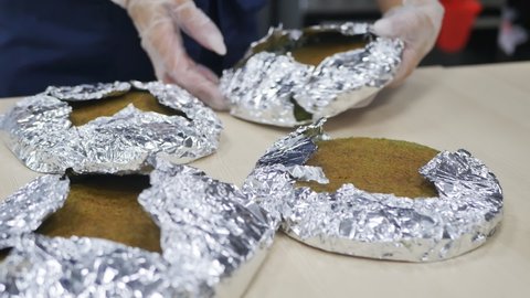 woman pastry chef piles baked foil-wrapped cakes in a pile one on top of the other. For cooling