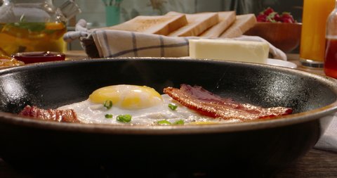 Putting frying pan with freshly fried eggs and bacon on table with served nourishing balanced breakfast - morning meal preparation 4k footage