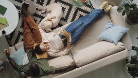 High angle shot of woman lying on sofa, reading book and petting dog as her African American husband browsing the web on smartphone while spending time together at home - Powered by Shutterstock - Get 15% off with code: PIKWIZARD15