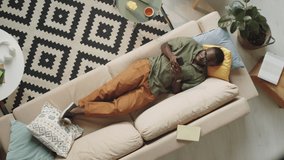 Top down shot of African American man in casual outfit and glasses lying on couch in living room and using smartphone - Powered by Shutterstock - Get 15% off with code: PIKWIZARD15