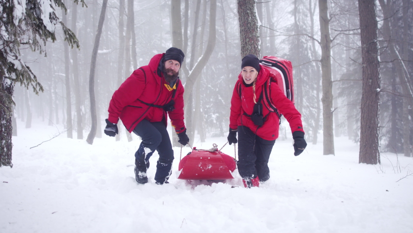 Mountain rescue service provide operation outdoors in winter in forest, pulling injured person in stretcher.