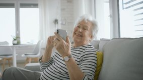 Senior woman at home with smartphone having an video call and laughing.