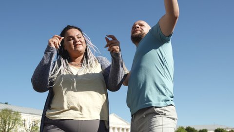 Music and copy space concept. man with tattoo and a woman with dreads dancing. Two young happy people dance on background of bright blue sky. Body positive fat friends enjoy life and sunny weather.