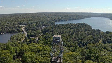 Time lapse drone shot approaching fire lookout tower over lake with boats and cars driving in village in background