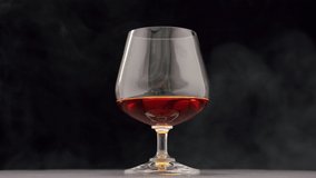 A drop of brandy falls into a glass of strong alcohol on a black background