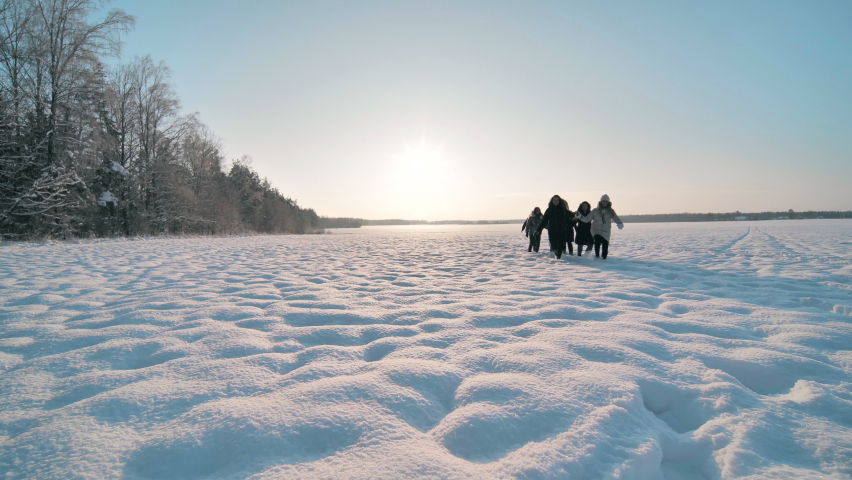 Cheerful girls run hand in hand across a snowy field.