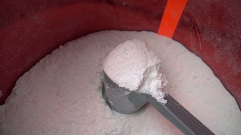 Filming an extreme macro, moving away from a measuring cup with white protein bcaa powder, glutamine, in a tank. Top view.