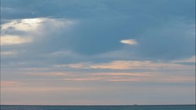 Dark blue clouds glide sideways low above the sea as the sun sets.  Sunlight penetrate through the cracks in the clouds. Sea ship sail fast along horizon line. Time lapse video.