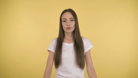 Portrait of a cute attractive woman 40 years old on an isolated yellow background in the studio. Long-haired woman in basic white t-shirt meditates over the proposal of the touching chin