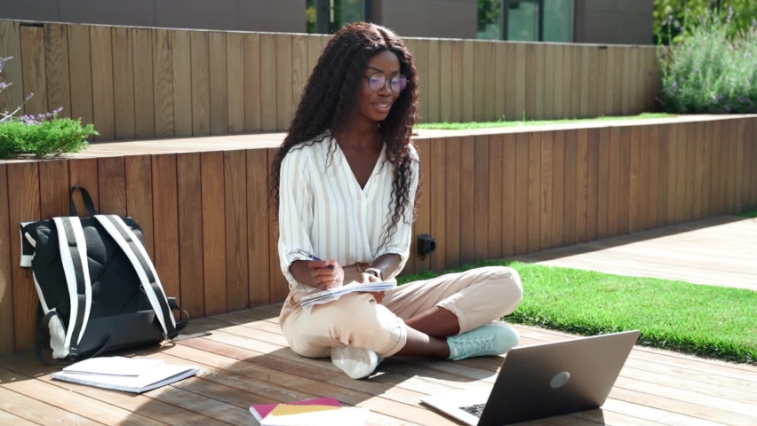 Young happy black African woman university student learning online using laptop computer having virtual education remote class training seminar studying outdoor sitting outside uni campus area. | Shutterstock HD Video #1080090410