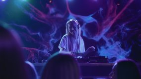 DJ plays disco music on turntable at night club scene. Partying joyful crowd moves in hip-hop rhythm of funky dance. Trendy girl in bright spot light of multi-color neon. Female dj at festival stage - Powered by Shutterstock - Get 15% off with code: PIKWIZARD15