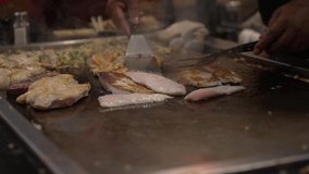 This video shows a hibachi chef flipping grilled fish fillets on a grill filled with delicious and fresh cooking food.