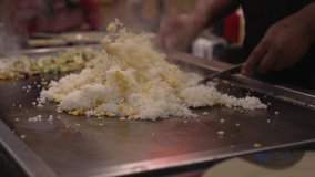 This close up video shows fried rice being stirred and cooked by a chef on a hibachi grill.