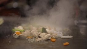 This video shows a large pile of fresh, mixed vegetables being stirred on a hibachi grill in slow motion.