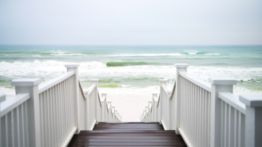 Man walking down downstairs wooden boardwalk stairs steps leading to Santa Rosa Beach Seaside, Florida panhandle town village with storm stormy ocean sea waves crashing on coast shore