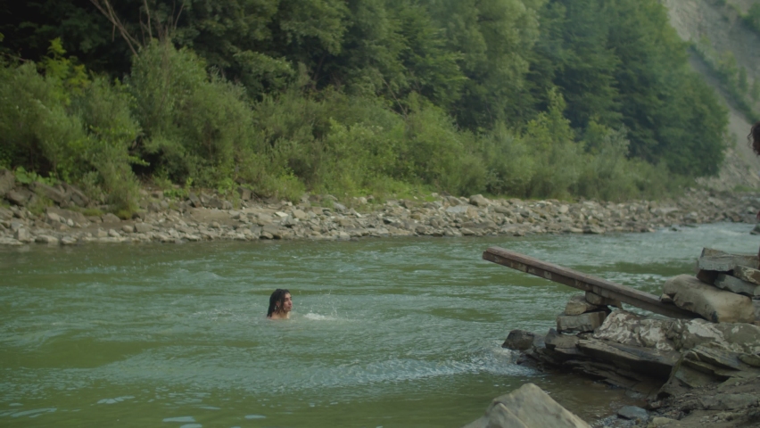 Carefree excited diverse multicultural people diving into mountain river off wooden springboard, having fun, swimming, enjoying recreation and freedom while friends relaxing on summer vacations.