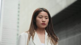 Confident Asian businesswoman wearing white suit walking among office buildings ambitious woman slow motion clip