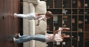 Vertical video energetic mom little daughter jump on floor with heating at living room of new cozy flat celebrate moving day have fun. Joyful young single mum preteen girl dance enjoy weekend at home