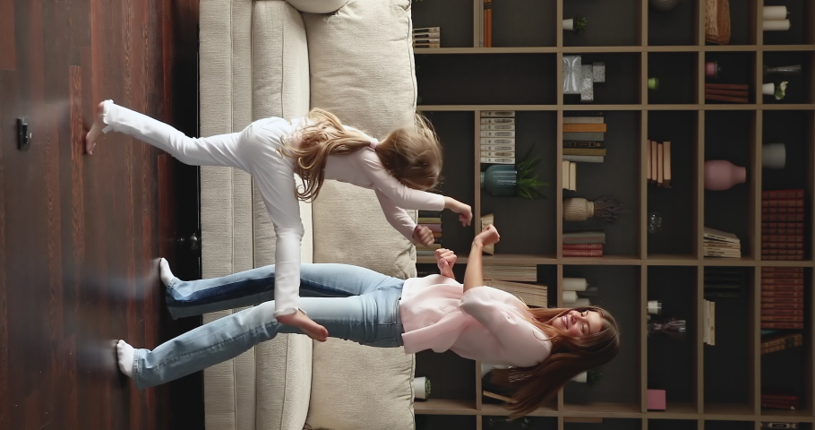 Vertical video energetic mom little daughter jump on floor with heating at living room of new cozy flat celebrate moving day have fun. Joyful young single mum preteen girl dance enjoy weekend at home Royalty-Free Stock Footage #1080107921