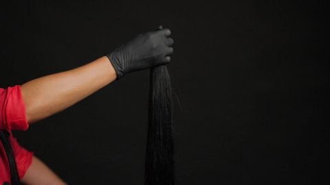 Preparation for hair extension. Girl holding hair in her hand on a black background close-up.