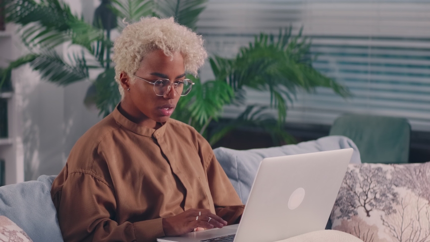 Angry upset young African American woman using laptop feel frustrated mad about computer problem, stressed about mistake software error worried reading bad news in social media sit on couch at home. | Shutterstock HD Video #1080111002
