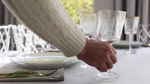 A waiter serves a table in a restaurant. Someone is setting the table in a restaurant. Plates and glasses are placed on the table. The decor of the festive table in gray-silver tones with gold cutlery