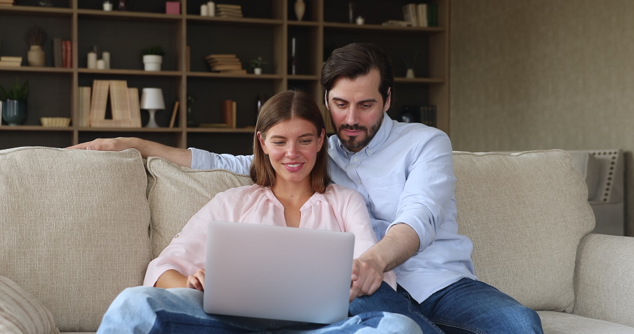 Excited young couple in love sit on couch read great news on laptop screen scream raise hands celebrate success. Happy emotional husband wife feel euphoric winning lottery prize getting loan approval Royalty-Free Stock Footage #1080114227