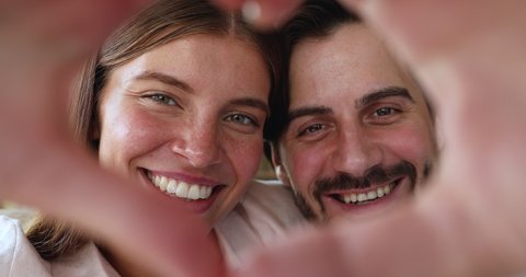 Enamored man woman happy couple in love looking at camera through tender heart of united hands. Webcam portrait of loving young spouses influencers sharing romantic story with audience in video blog