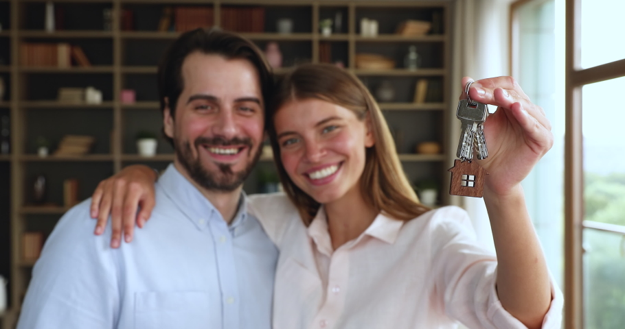 Excited young married couple newlyweds first time buying house receiving mortgage loan hugging looking at camera holding bunch of keys. Portrait of laughing spouses real estate owners in new apartment | Shutterstock HD Video #1080114266