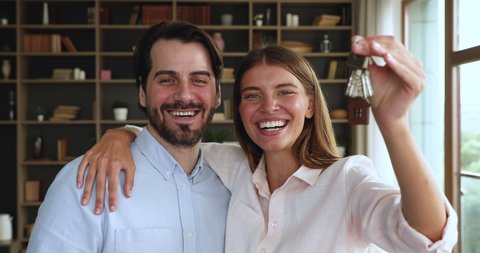 Excited young married couple newlyweds first time buying house receiving mortgage loan hugging looking at camera holding bunch of keys. Portrait of laughing spouses real estate owners in new apartment