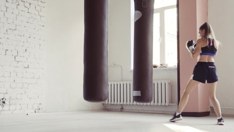 Female athlete boxing the punching bag in urban industrial gym