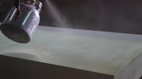 worker paints a board with a spray gun at a furniture factory