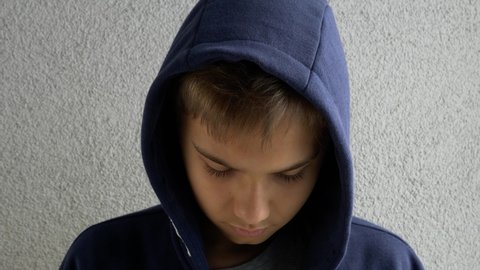 Teenage boy in navy hooded jacket raises his head and looking directly to camera. Calm, serious, sad, contemplative kid. Close up candid portrait. 4k video