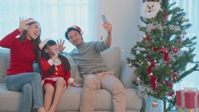 Asian Parent and daughter wear Santa hat video call online with family. Loving father, mother and young girl child using mobile phone and talk to relative during holiday Christmas Thankgiving in house