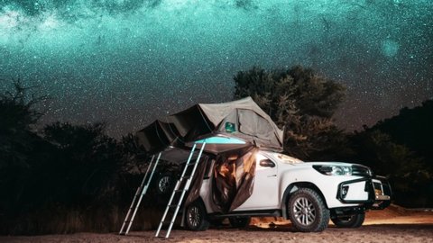 Astronomy Namibia starry landscape, travel in galaxy. Night timelapse of a safari vehicle in an adventurous wild camping location with a rooftop tent against the Milky Way and starry sky.