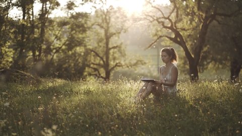Girl sitting in park or forest, opening laptop on nature. IT specialist working at self isolation outdoors. Woman engaging in business or freelance at nature or fresh air at amazing sun light.