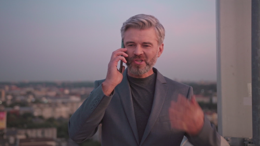 Serious businessman speak on mobile phone on roof top at city skyscraper. Slow motion