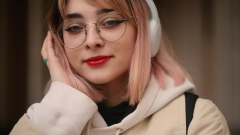 Slow motion of smiling young girl with pink hair listening to music in headphones at the university. Closeup face of beautiful young girl with short pink hair.