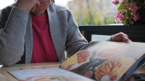 Close-up of a woman leafing through pages in a restaurant or cafe menu.