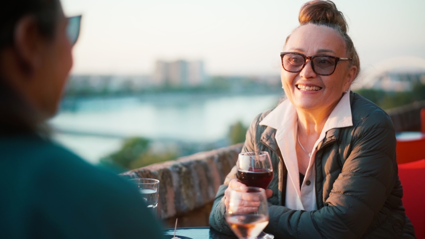 Happy beautiful mature woman in glasses sitting in a cafe with her daughter and drinking wine.