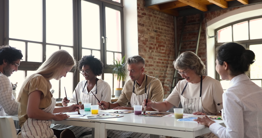 Six different age and ethnicity artist people engaged in painting art class in workshop, sit at table drawing on paper with watercolour. Creative hobby and education, develop skills and talent concept