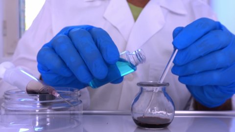 A research lab technician mixes chemical ingredients in a glass jar.