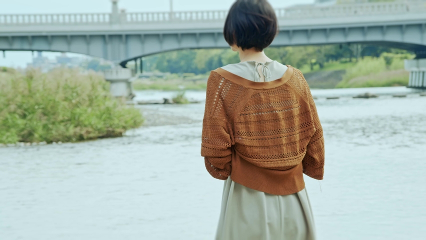 A woman with short hair looking at a bridge over a river.